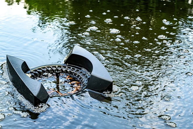 A floating pond skimmer collecting debris and leaves in a backyard pond - Grass Roots Pond And Garden A floating pond skimmer collecting debris and leaves in a backyard pond